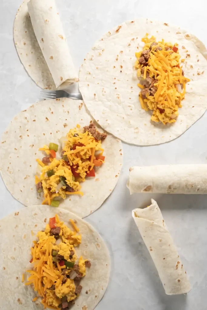 Step by step assembly of homemade breakfast burritos with scrambled eggs, sausage, vegetables, and shredded cheddar cheese on flour tortillas.