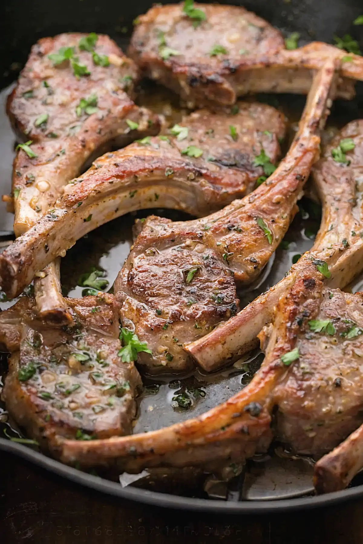 Pan seared lamb chops in a skillet with garlic butter sauce and fresh parsley garnish