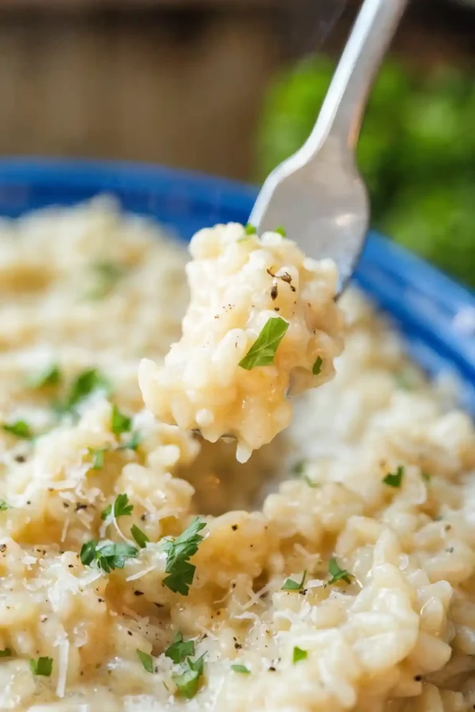 Spoon lifting creamy parmesan risotto from a bowl, topped with grated parmesan, chopped parsley, and black pepper.