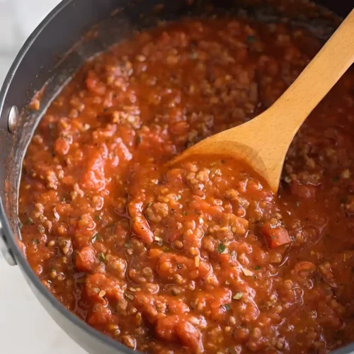 spaghetti meat sauce simmering in pan with wooden spoon