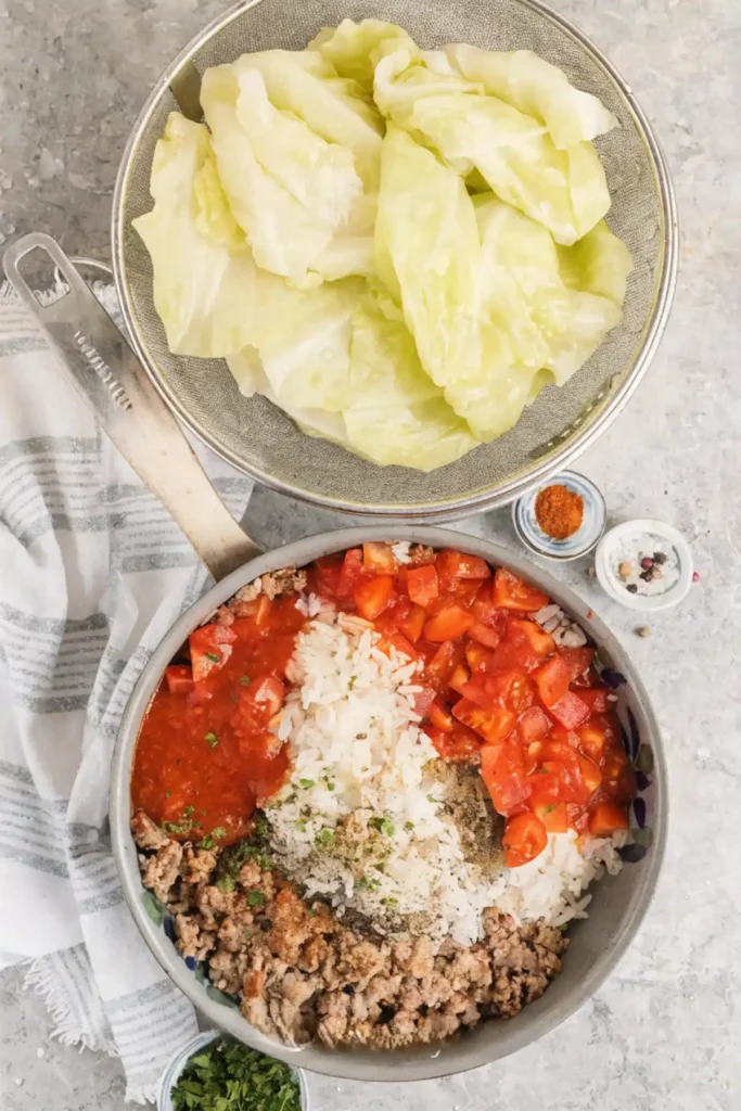 Ingredients for stuffed cabbage rolls including cabbage leaves, ground meat, rice, diced tomatoes, and tomato sauce in a skillet.