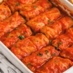Baked cabbage rolls in tomato sauce served in a white casserole dish with fresh parsley garnish.