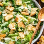 Caesar salad recipe with romaine lettuce, crispy croutons, shaved parmesan, and creamy dressing in a white bowl