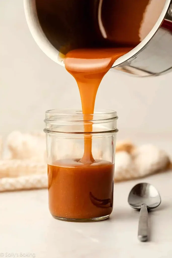 Caramel sauce being poured into a glass jar showing smooth thick texture and rich amber color