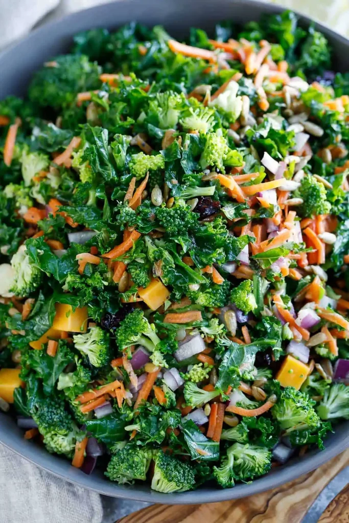 Healthy kale salad mixed with broccoli, carrots, red onion, seeds, dried cranberries, and cheese in a bowl with light dressing.