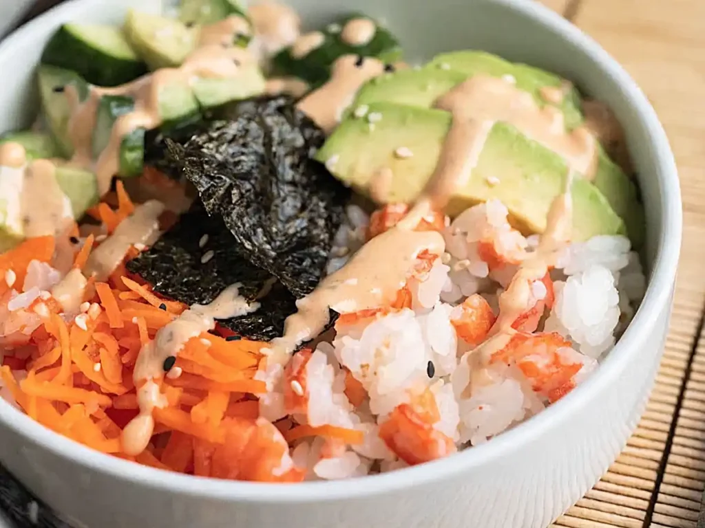 Healthy sushi bowl with crab, avocado, cucumber, carrot, rice, nori, and spicy mayo in a white bowl