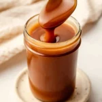 Homemade caramel sauce dripping from a spoon into a glass jar with smooth glossy texture