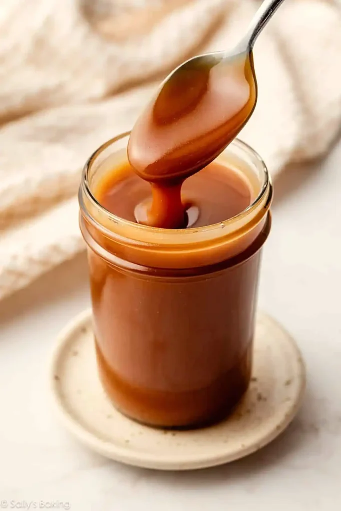 Homemade caramel sauce dripping from a spoon into a glass jar with smooth glossy texture