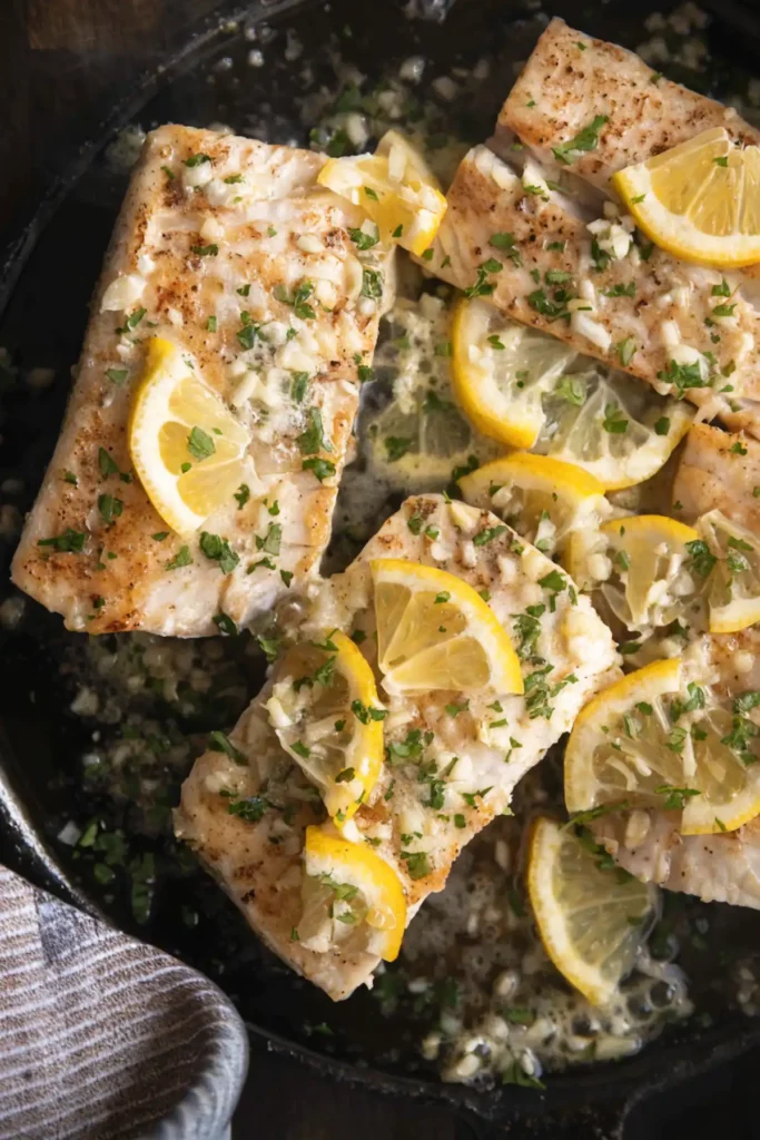 Pan-seared mahi mahi fillets in a skillet with lemon garlic butter sauce, fresh parsley, and sliced lemons.