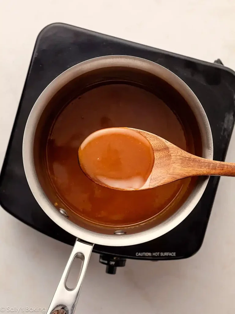 Caramel sauce cooking in a saucepan with a wooden spoon showing smooth amber texture