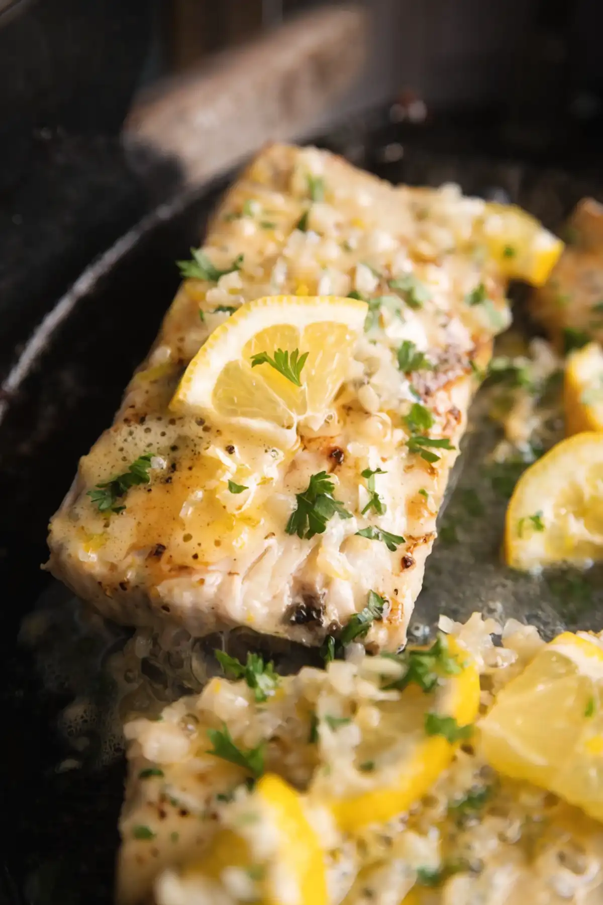 Pan-seared mahi mahi fillet with lemon garlic butter sauce, topped with fresh parsley and a lemon slice in a skillet.