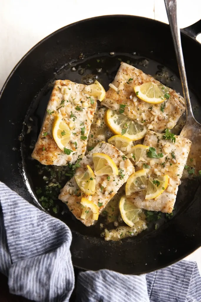Pan seared mahi mahi fillets in a skillet with lemon garlic butter sauce, parsley, and fresh lemon slices.