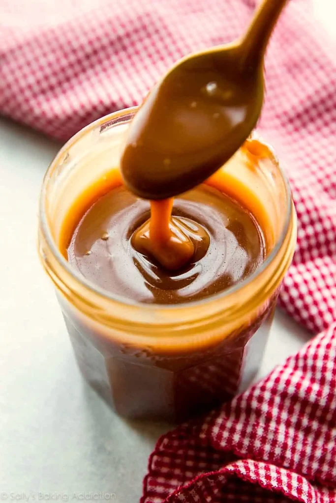 Salted caramel sauce in a jar with a spoon showing thick glossy texture and rich dark color