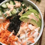 Sushi bowl with crab, avocado, cucumber, carrot, nori, and spicy mayo in a white bowl on a kitchen background