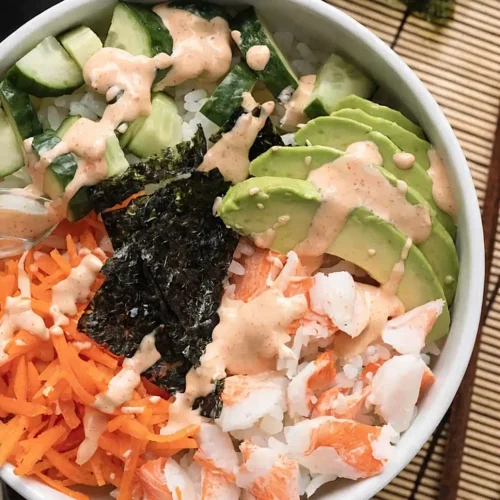Sushi bowl with crab, avocado, cucumber, carrot, nori, and spicy mayo in a white bowl on a kitchen background