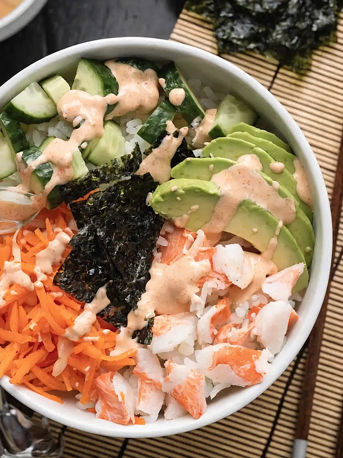 Sushi bowl with crab, avocado, cucumber, carrot, nori, and spicy mayo in a white bowl on a kitchen background