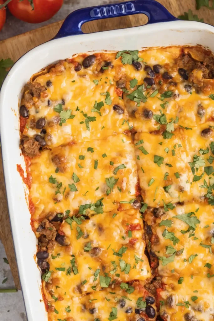 Top view of beef enchilada casserole with melted cheese, black beans, and fresh cilantro in a white baking dish
