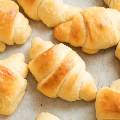 Fresh homemade crescent rolls baked golden brown on a parchment lined baking sheet with a soft buttery texture