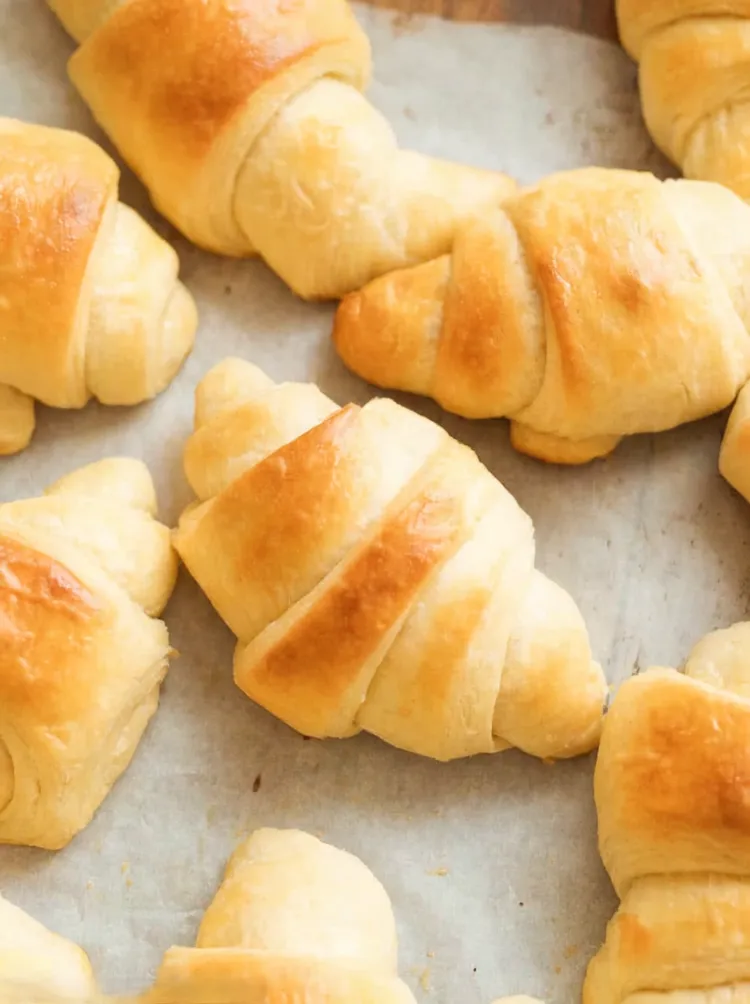 Fresh homemade crescent rolls baked golden brown on a parchment lined baking sheet with a soft buttery texture