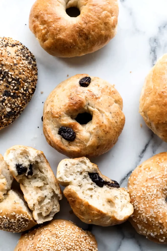 Assorted homemade bagels including plain, everything, sesame, sugar crusted, and cinnamon raisin bagels with some sliced to show a soft interior