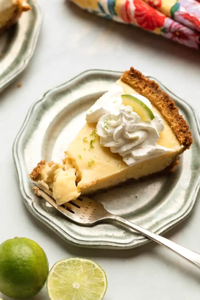 Easy key lime pie slice with whipped cream topping and lime on a plate with graham cracker crust