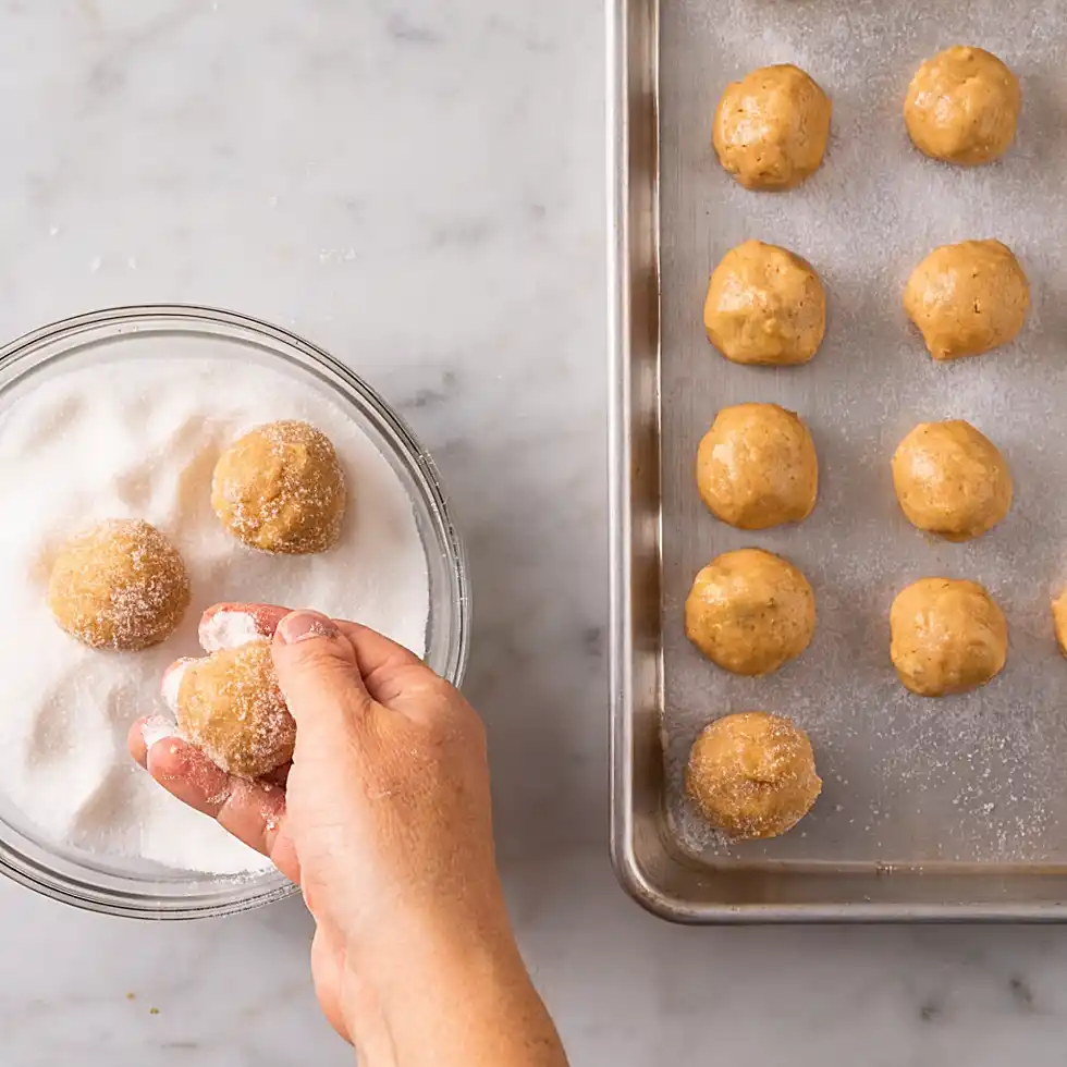 Rolling peanut butter cookie dough balls in sugar before baking blossom cookies