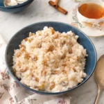 Creamy rice pudding with raisins and cinnamon in a blue bowl with tea in the background