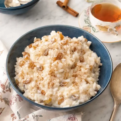 Creamy rice pudding with raisins and cinnamon in a blue bowl with tea in the background