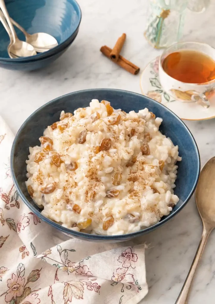 Creamy rice pudding with raisins and cinnamon in a blue bowl with tea in the background