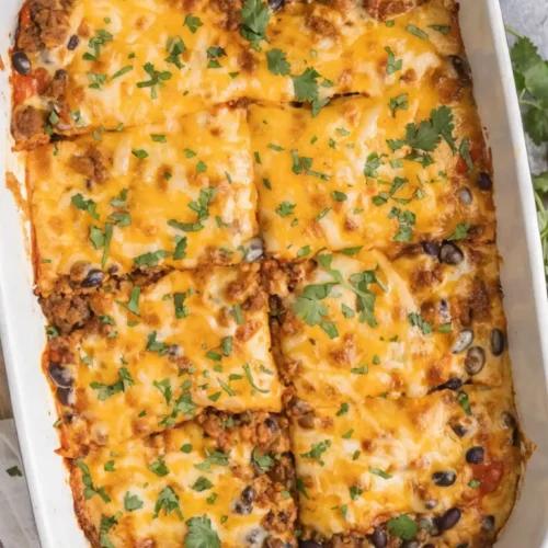 Cheesy beef enchilada casserole baked with black beans and topped with melted cheese and fresh cilantro in a white dish