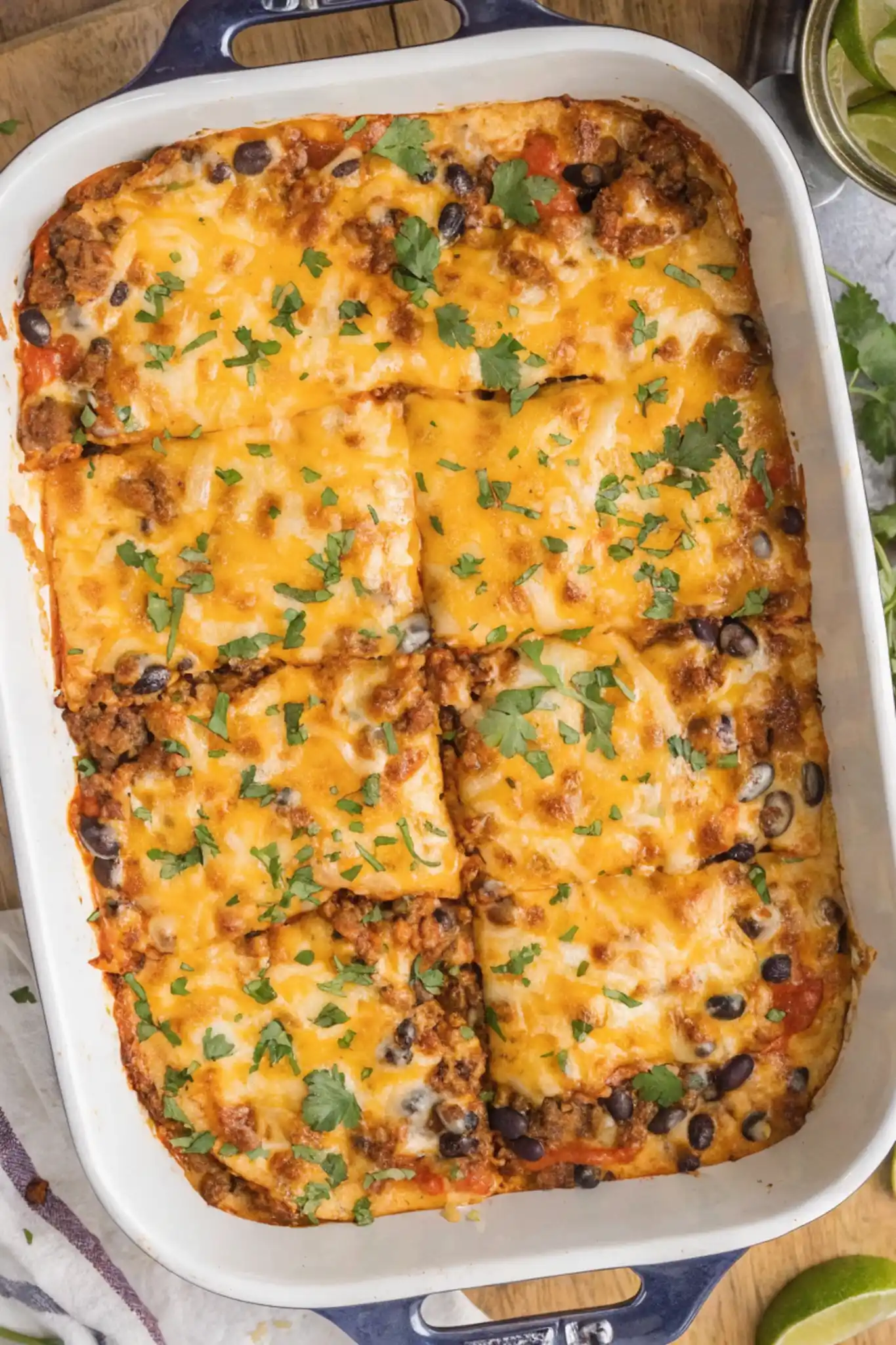 Cheesy beef enchilada casserole baked with black beans and topped with melted cheese and fresh cilantro in a white dish