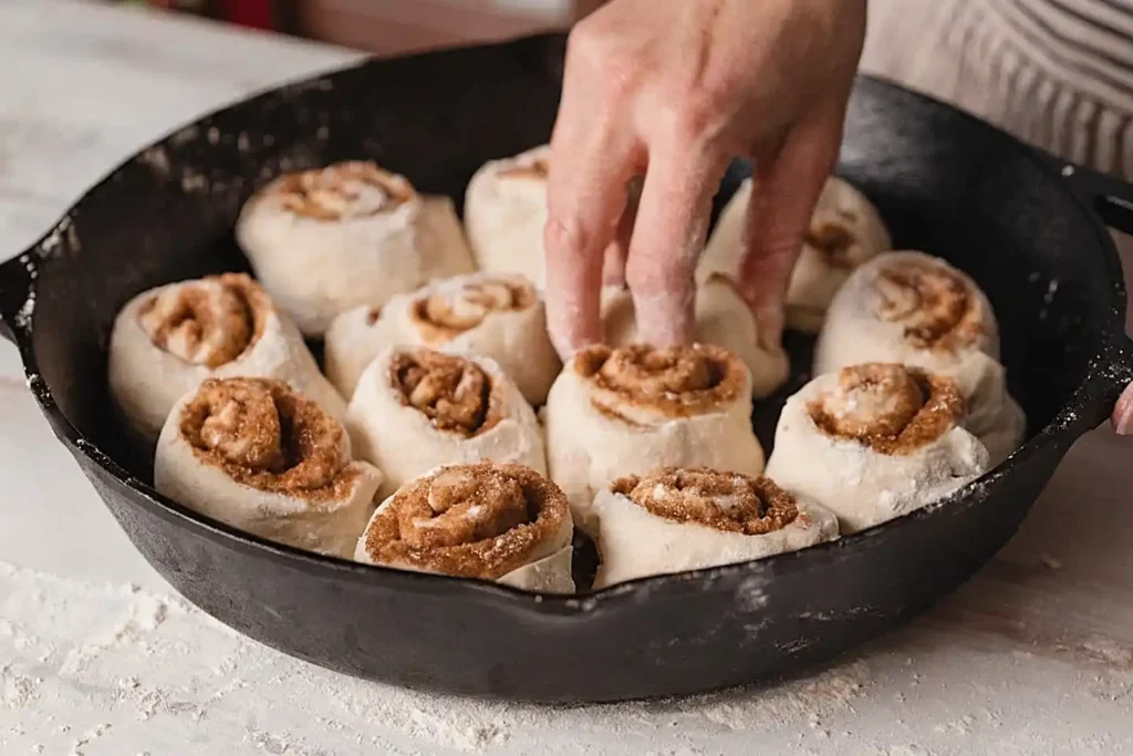 Sourdough cinnamon rolls being placed in a cast iron skillet before baking with visible cinnamon filling