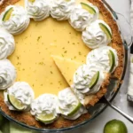 Key lime pie with whipped cream topping, lime slices, and graham cracker crust with a slice being served