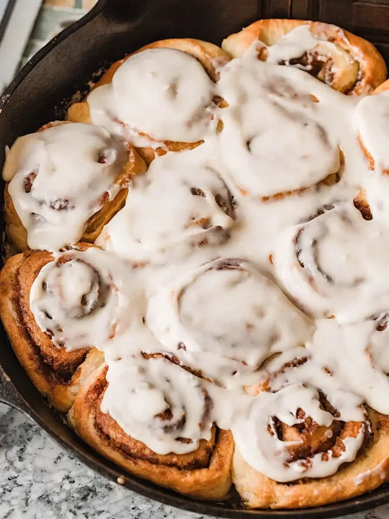 Overnight sourdough cinnamon rolls in a cast iron skillet topped with thick creamy glaze and golden swirls