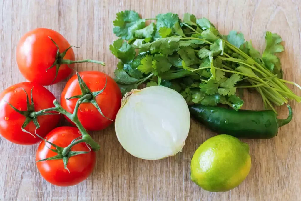 Fresh pico de gallo ingredients with tomatoes onion cilantro jalapeño and lime on a wooden surface