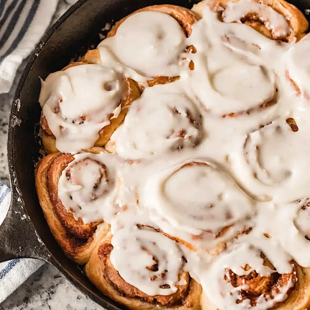 Sourdough cinnamon rolls in a cast iron skillet topped with creamy glaze and golden brown swirls
