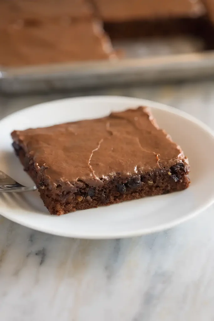 Best Texas sheet cake slice on a white plate with chocolate frosting and sheet pan in the background