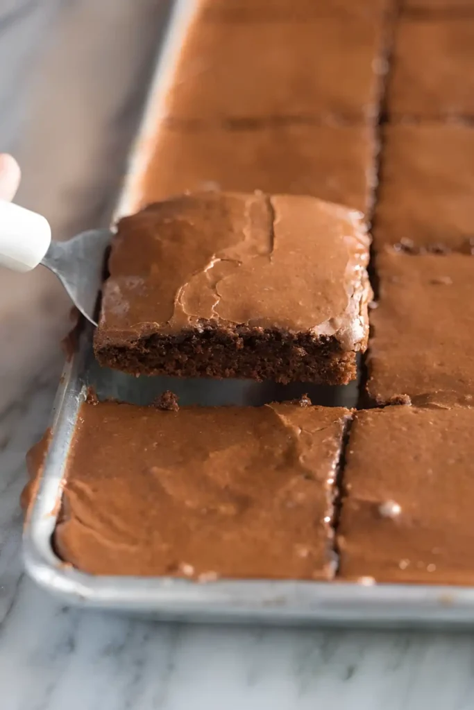 Texas sheet cake slice being lifted from a sheet pan with a spatula