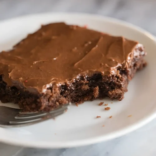 Slice of Texas sheet cake on a white plate with chocolate frosting and a bite taken out
