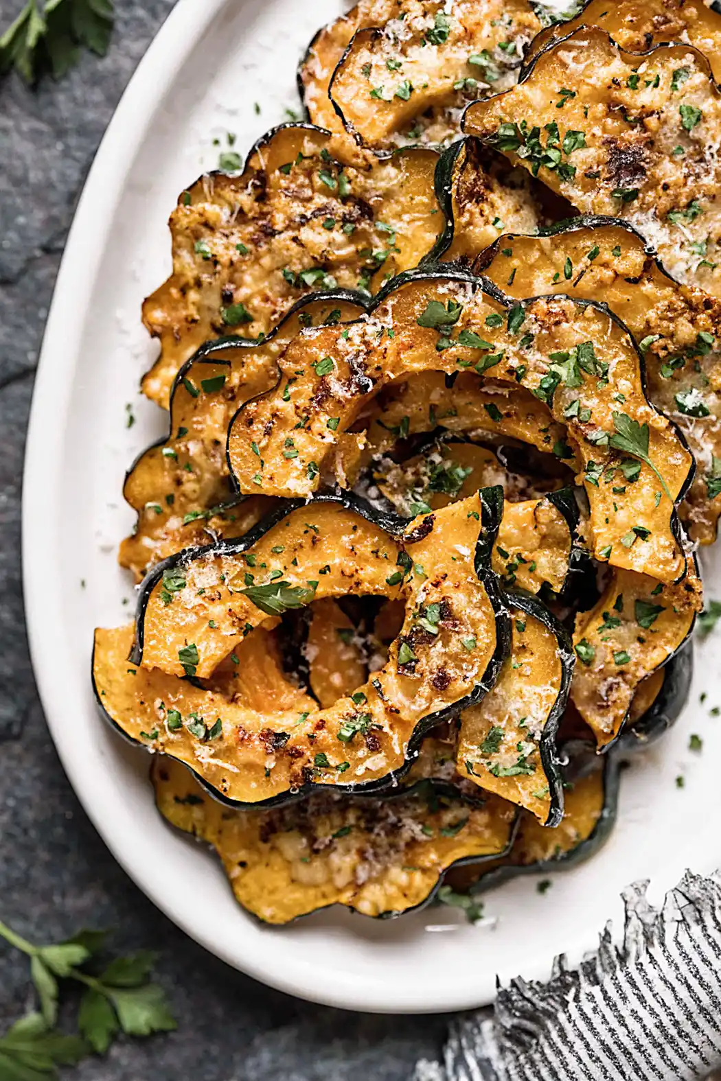 Easy acorn squash recipe served on a white platter with roasted Parmesan crusted acorn squash slices topped with fresh parsley.