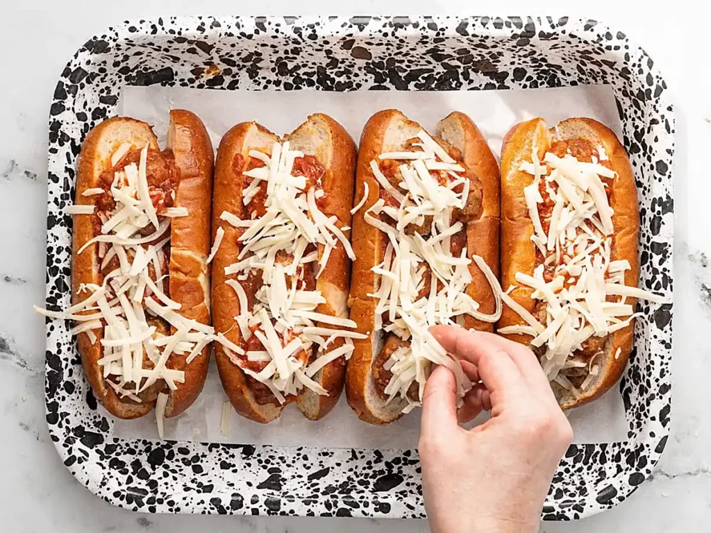 Easy meatball sub recipe with toasted hoagie rolls topped with shredded mozzarella before baking on a tray.