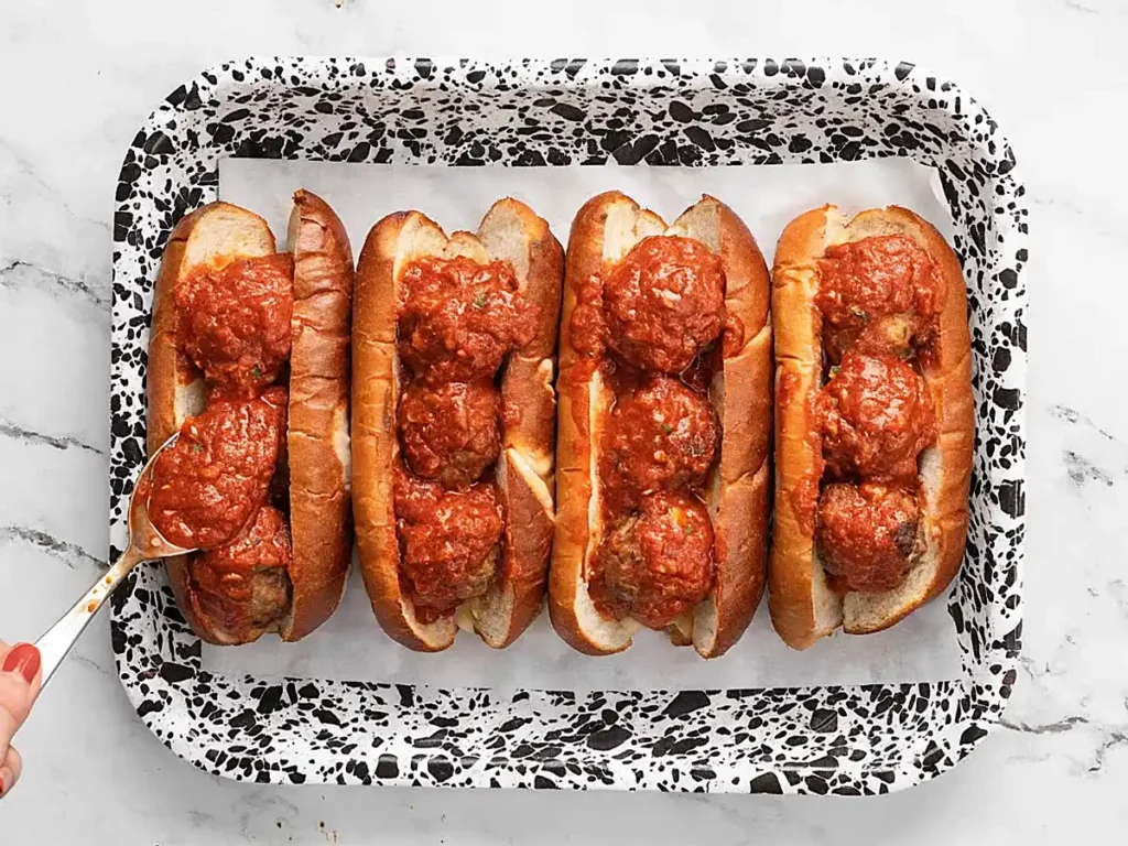 Meatball subs on a baking tray with toasted hoagie rolls, homemade meatballs, and marinara sauce before adding cheese.