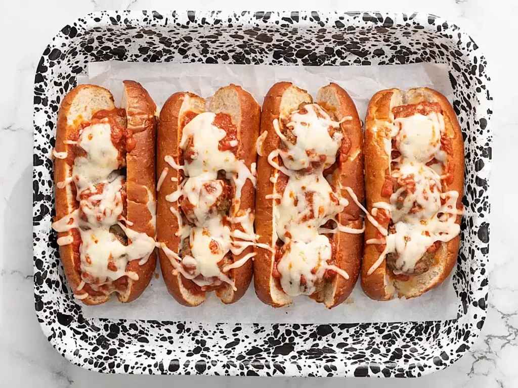 Meatball subs recipe baked with melted mozzarella cheese on toasted hoagie rolls served on a baking tray.