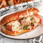 Slow cooker meatball sub on a plate topped with melted mozzarella cheese, marinara sauce, and fresh parsley in a toasted hoagie roll.