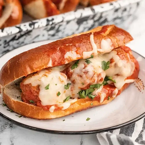 Slow cooker meatball sub on a plate topped with melted mozzarella cheese, marinara sauce, and fresh parsley in a toasted hoagie roll.